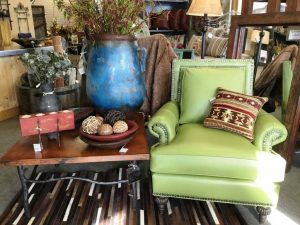 Image of furnishings showroom with green armchair and blue vase on wood and iron table